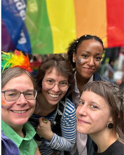 CSD Selfie mit vier Kolleginnen  und Regenbogenflagge im Hintergrund